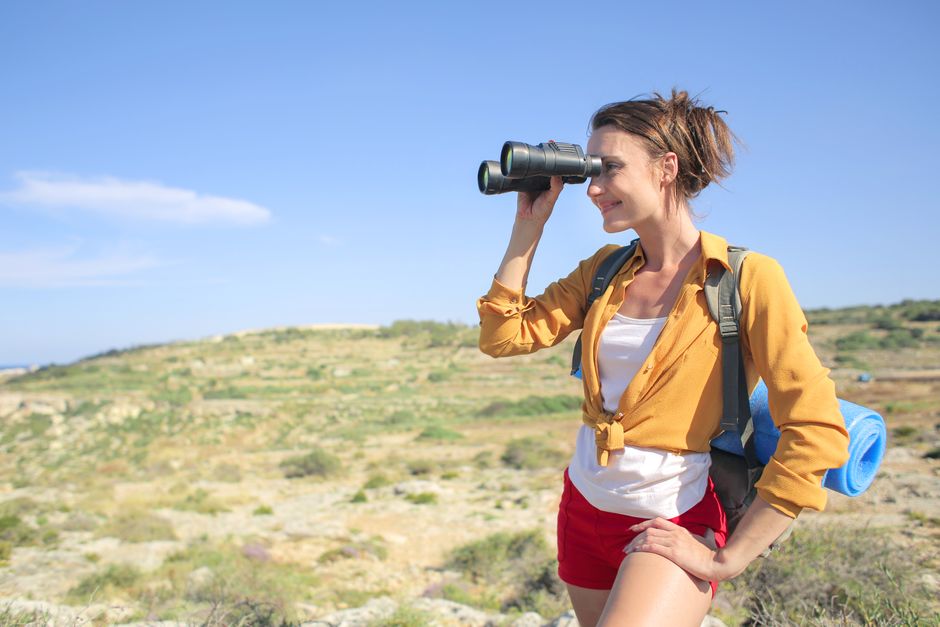 Young woman enjoying a sunny day hike, using binoculars to explore nature and capture the scenic view.